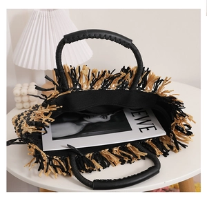 Detail of two-tone woven straw tote bag with fringe edge and leather handles