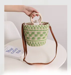 Détail d'un sac seau en paille tressée verte avec poignées en bois et bandoulière en similicuir