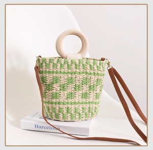 Détail du sac seau en paille à carreaux verts avec poignée en bois sur chaise