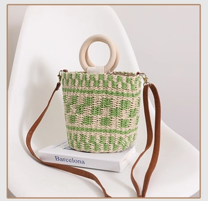 Détail du sac seau en paille à carreaux avec anses en bois sur une chaise blanche