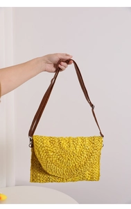 Detail of yellow woven straw envelope bag with textured finish and brown shoulder strap