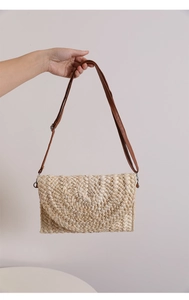 Detail of hand-woven straw bag with beige texture and brown leather strap on white background