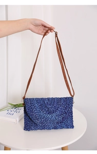 Detail of navy corn husk woven bag with brown leather strap and fold-over flap closure