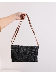 Close-up of black corn husk woven crossbody bag with brown leather strap and texture detail