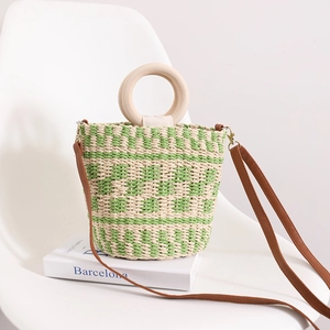 Sac seau en paille vert et blanc avec poignée ronde en bois et bandoulière en cuir sur chaise