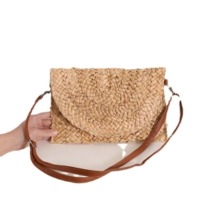 Handmade corn husk straw crossbody bag with brown leather strap and woven flap texture