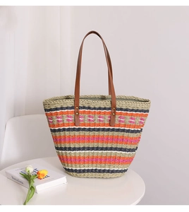 Detail of colorful striped straw tote bag with brown leather handles on a white table
