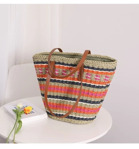 Detail of multi-color striped straw tote bag with brown leather handles on a white table
