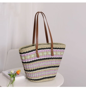 Close-up of a striped straw tote bag with brown leather handles on a white table