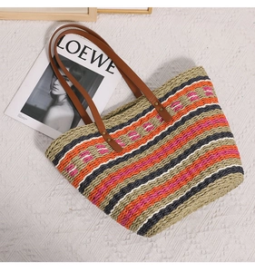 Close-up of multicolor striped straw tote bag with brown leather handles on a beige rug