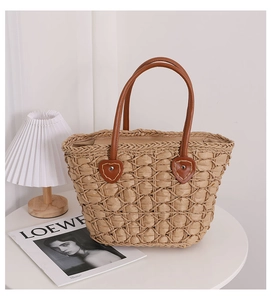 Detail of woven straw tote bag with heart leather patches and brown handles on table
