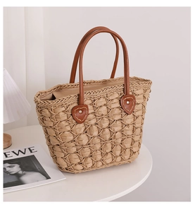 Detail of diamond weave straw tote bag with brown leather handles and silver studs