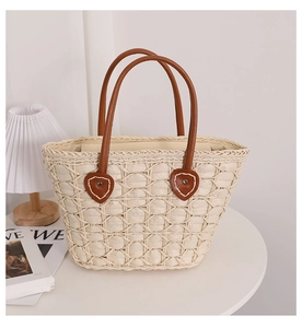 Detail of heart-shaped leather patch and stitching on beige straw tote bag with brown straps