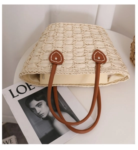 Macro detail of beige woven straw tote featuring heart-shaped leather strap attachments