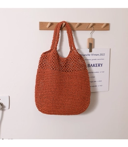 Detail of bohemian burnt orange woven tote bag hanging on a minimalist wooden hook