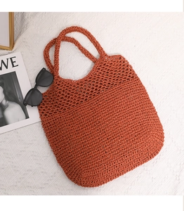 Detail of rust-red hollow straw tote bag showing intricate knit texture and handle