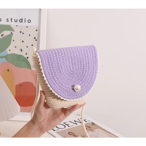 Detail of hand-woven purple and beige straw bag featuring a pearl closure and mini pom-poms