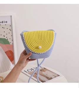 Close-up of blue and yellow woven straw bag featuring white pom-pom trim and pearl buckle