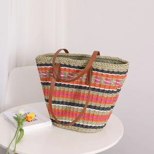Colorful striped straw tote bag with brown leather handles on a white table
