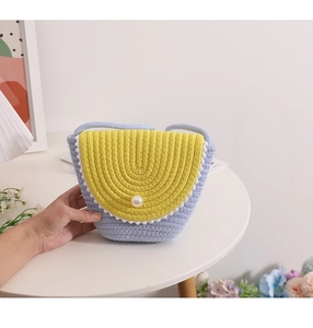 Detail of blue and yellow straw bag with pom-poms and a central pearl closure