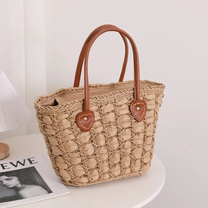 Handwoven khaki straw tote bag with brown leather handles in a clean lifestyle setting