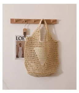 Detail of hollow woven straw tote bag in beige hanging on a wooden wall hook