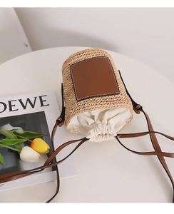 Detailansicht der Raffia-Eimertasche mit braunem Lederriemen und weißem Kordelzug-Innenbeutel