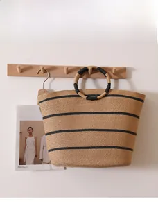 Detail of a large striped straw tote bag hanging on a wooden rack with circular handles