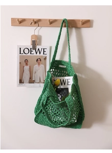 Detail of green hollow mesh woven straw tote bag hanging on a minimalist wooden peg