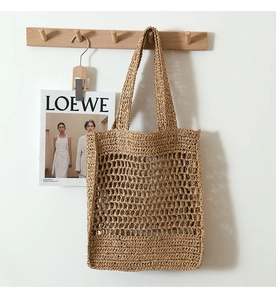 Detailed close-up of dark beige hollow mesh straw tote bag hanging on a wooden wall hook