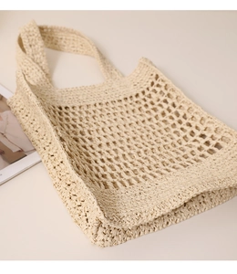 Close-up of beige woven mesh tote bag with wide shoulder strap on minimalist surface
