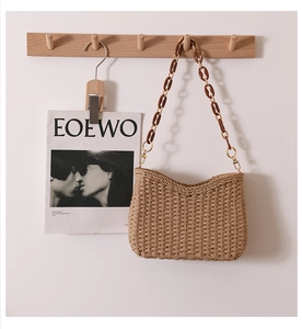 Close-up of woven straw shoulder bag with amber-style resin chain and gold hardware