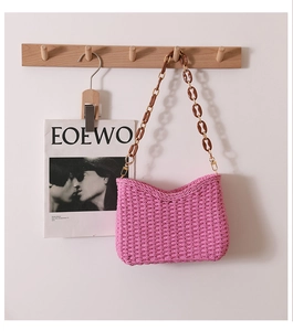 Detailed texture of pink woven shoulder bag with amber acrylic chain on a wooden hook
