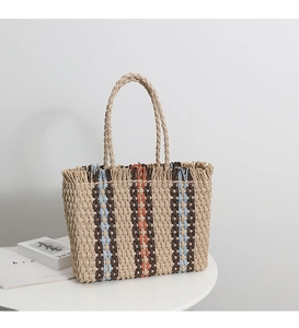 Detailed close-up of vertical striped straw tote bag with fringe edge and woven handles