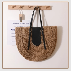 Detail of a large half-moon straw tote bag with black leather patchwork and contrast stitching