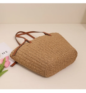 Détail latéral d'un sac cabas en paille avec anses en cuir marron et surpiqûres blanches