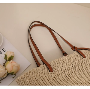 Gros plan du sac cabas en paille avec anses en cuir marron et coutures blanches décoratives