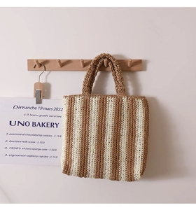 Detailed close-up of a striped French straw woven tote bag hanging on a wooden hook