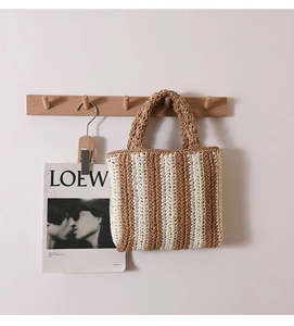 Vertical striped straw tote bag in beige and brown hanging on a rustic wooden hook
