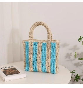 Detail of hand-woven vertical striped straw tote bag in beige and blue on a table