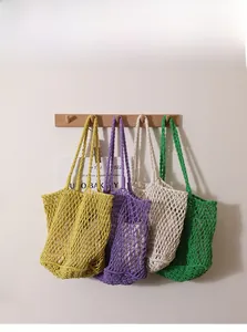 Detail of multi-color woven cotton net bags hanging on hooks in a minimalist setting