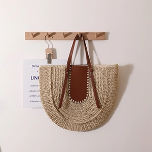 Large half-round straw tote bag with brown leather handles hanging on a hook