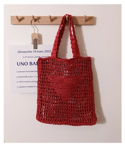 Close-up of red hollow crochet tote bag with a woven heart pattern and mesh texture