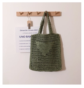 Detail of green crochet straw tote bag with textured heart embroidery on woven material