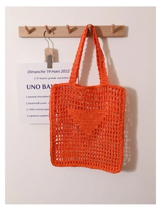 Detail of an orange crochet tote bag with a hollow woven grid on a wooden hook