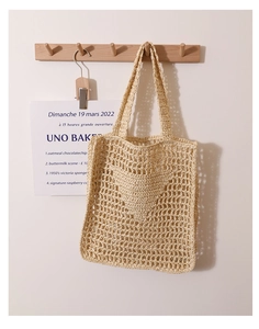 Detail of hand-woven beige crochet shoulder bag with hollow mesh texture on a wooden hook