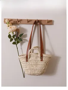 Detail of handmade woven straw tote bag with brown leather straps hanging on a wall hook