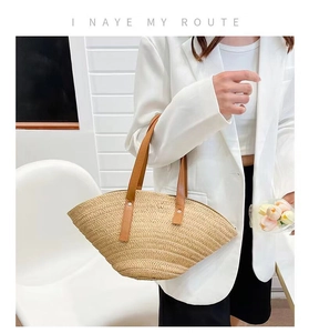 Detail of hand-woven straw beach bag featuring brown leather handle and metal rivets