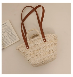 Detail of straw tote bag with brown faux leather straps and natural woven texture