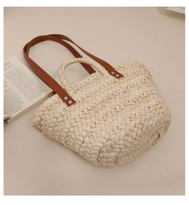 Detailed close-up of natural corn husk weaving and brown leather straps on a tote bag